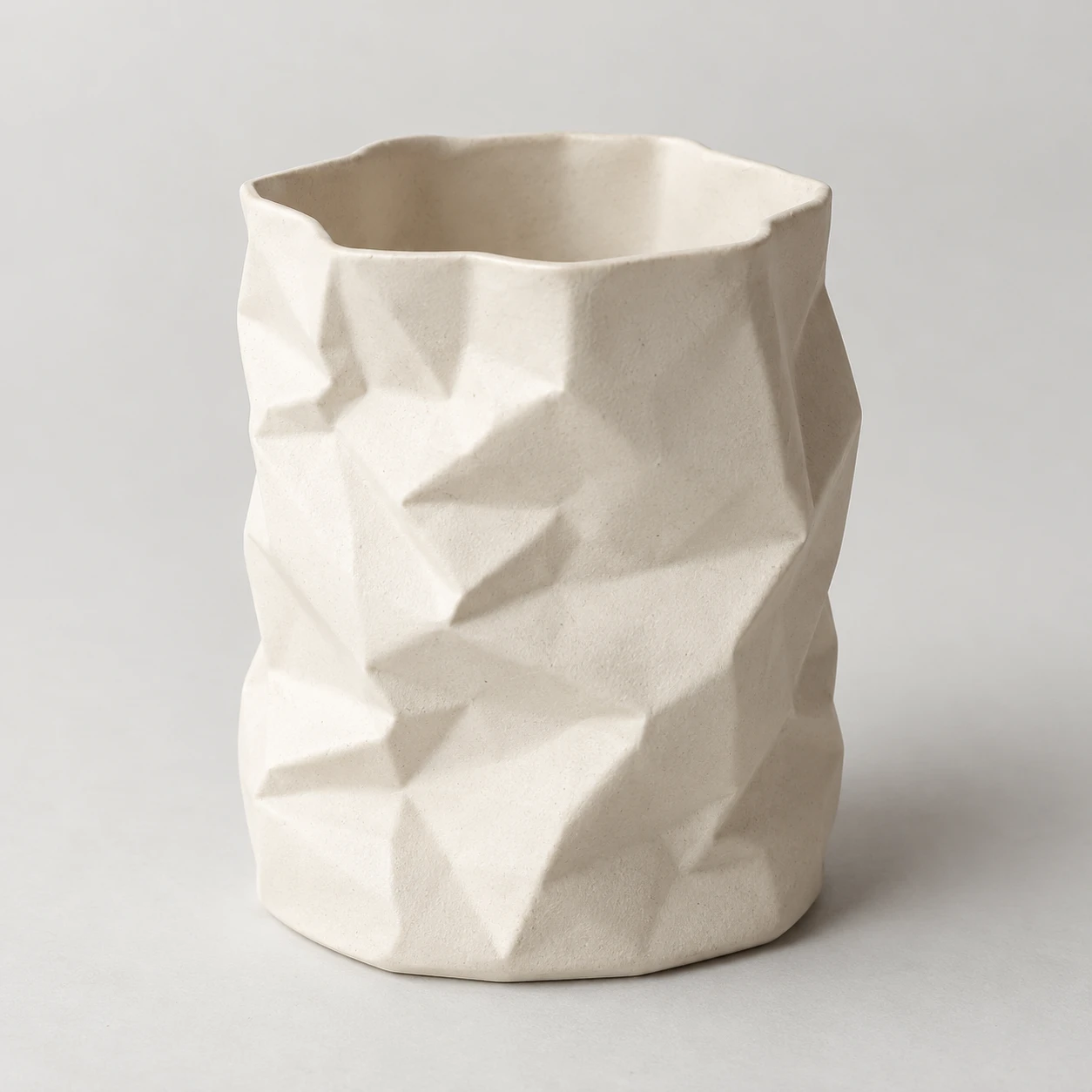 Empty ivory ceramic pencil pot with angular crumpled-paper folds.