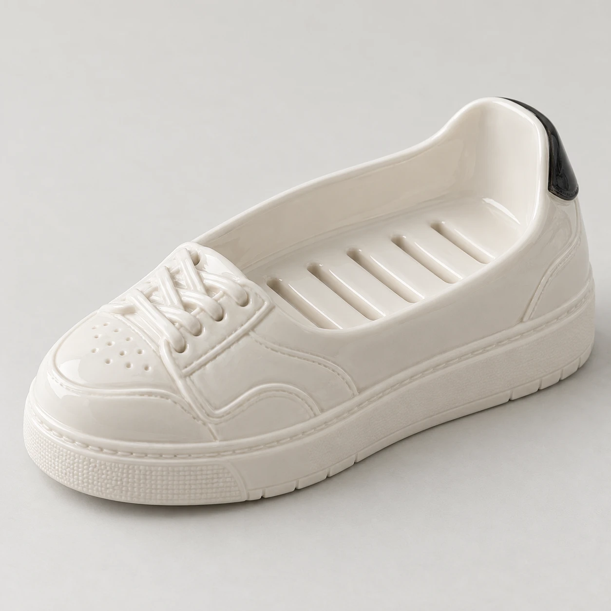 White ceramic sneaker-shaped soap dish with drainage slots and a black heel detail.