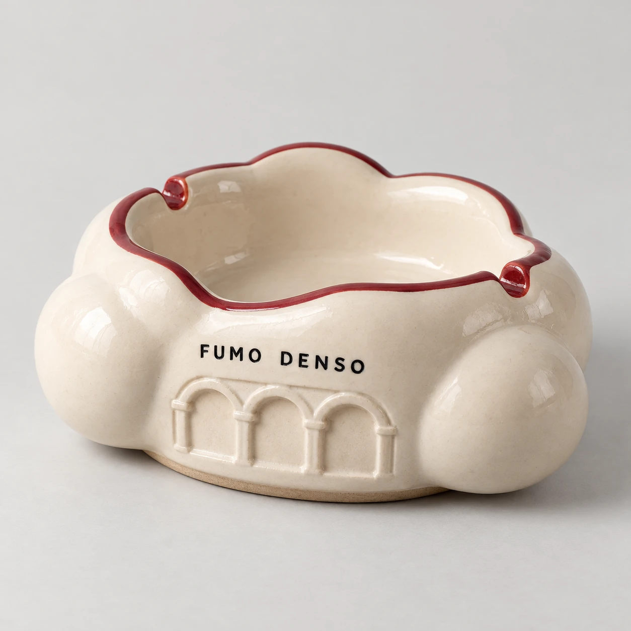Cream cloud-shaped ceramic ashtray with a dark red rim, portico relief and Fumo Denso lettering.