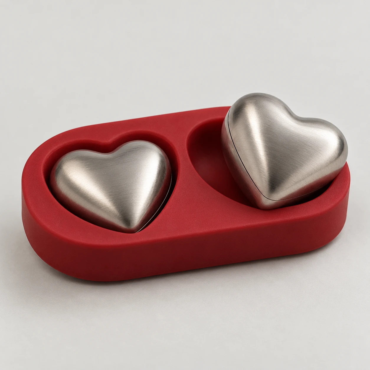 Two heart-shaped steel drink chillers in a red silicone tray.