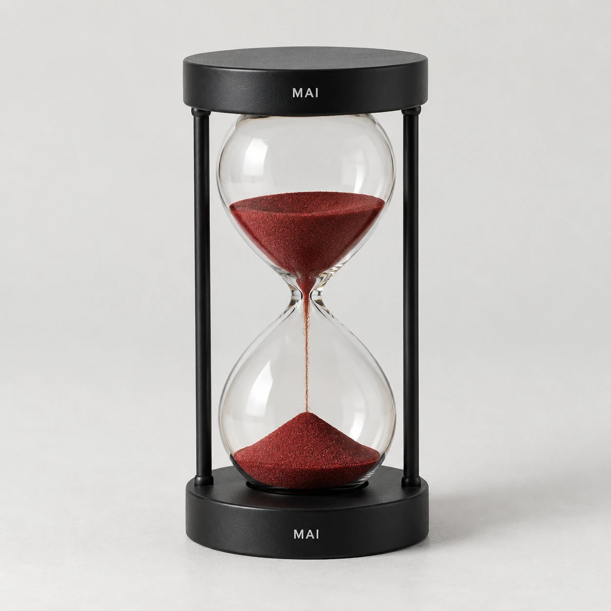 Black-framed hourglass with dark red sand and MAI lettering on both endcaps.