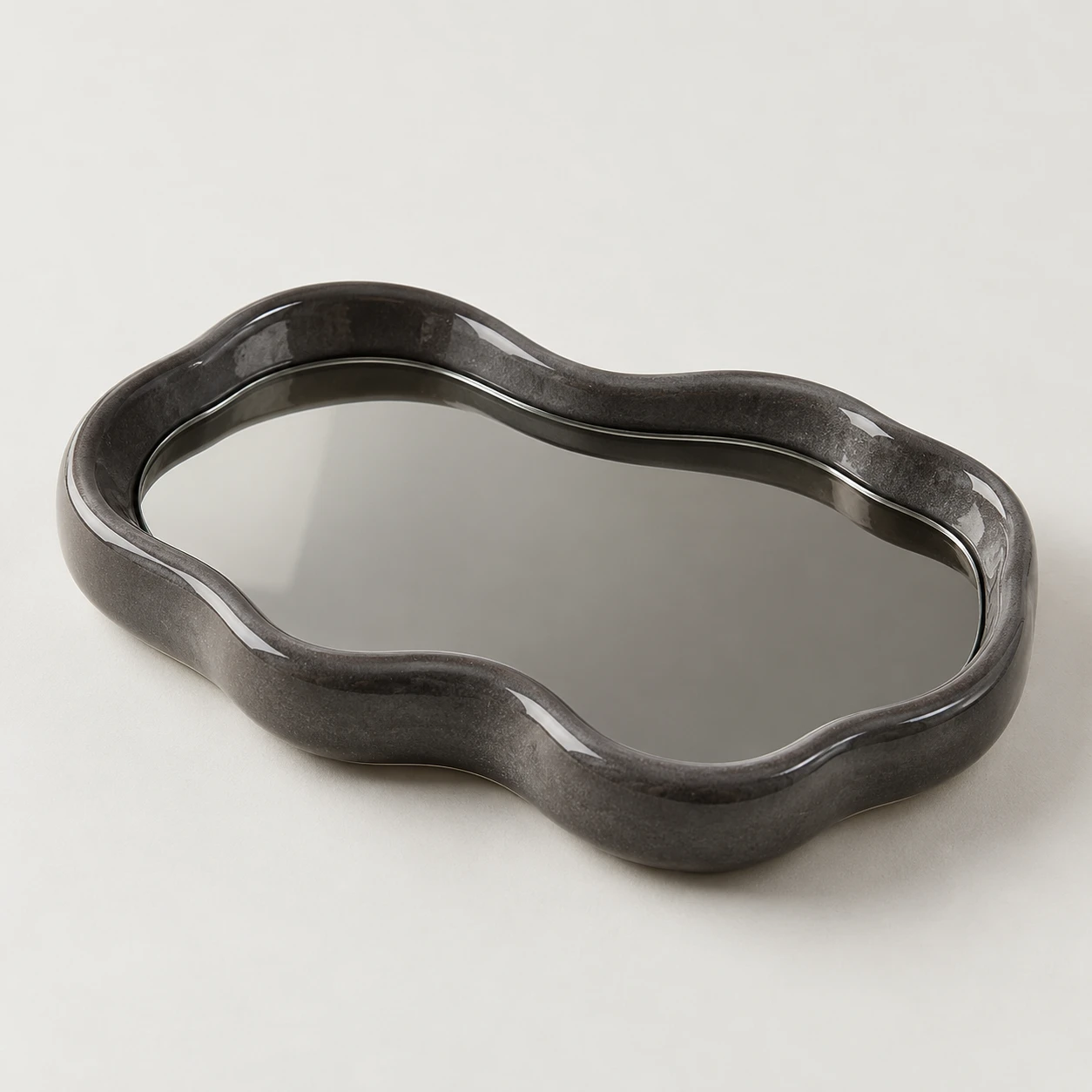 Puddle-shaped tray with a charcoal ceramic rim and reflective smoked-glass center.