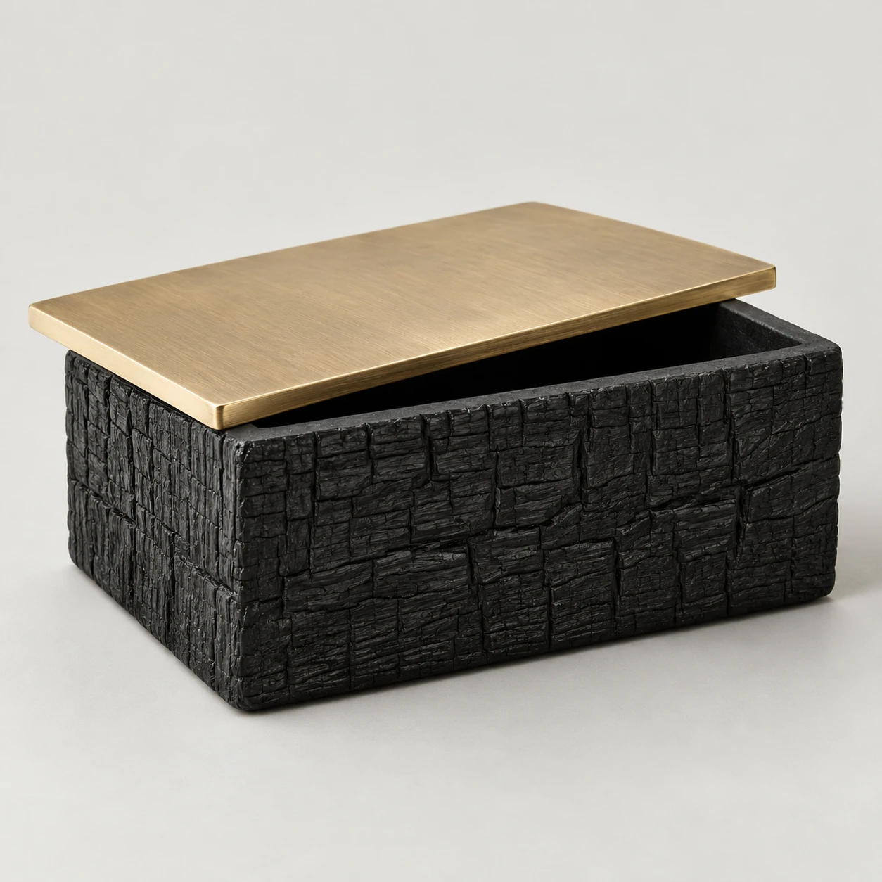 Black ceramic keepsake box with charred-wood texture and a partly open brass lid.
